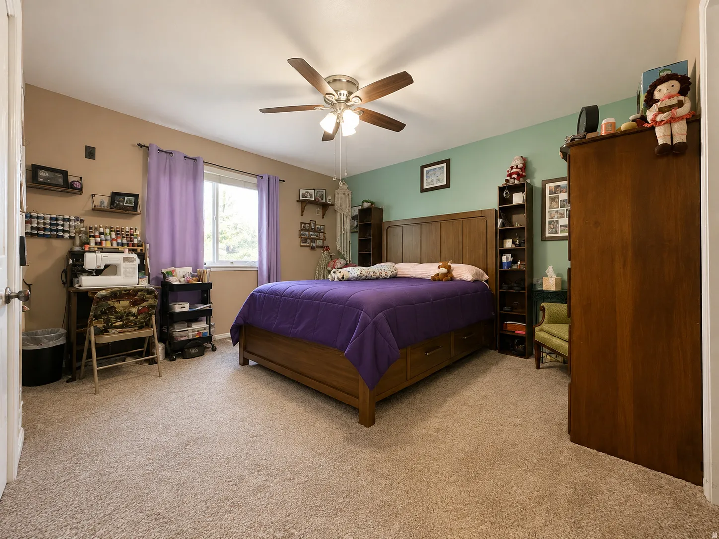 Plush carpet flooring, ceiling fan with integrated lighting, and a large window providing ambient light