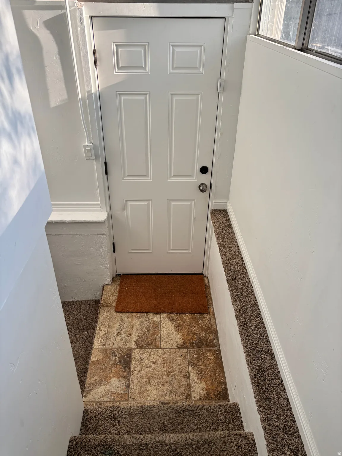 Six-panel entry door with polished hardware, textured tile flooring, and carpeted stairs