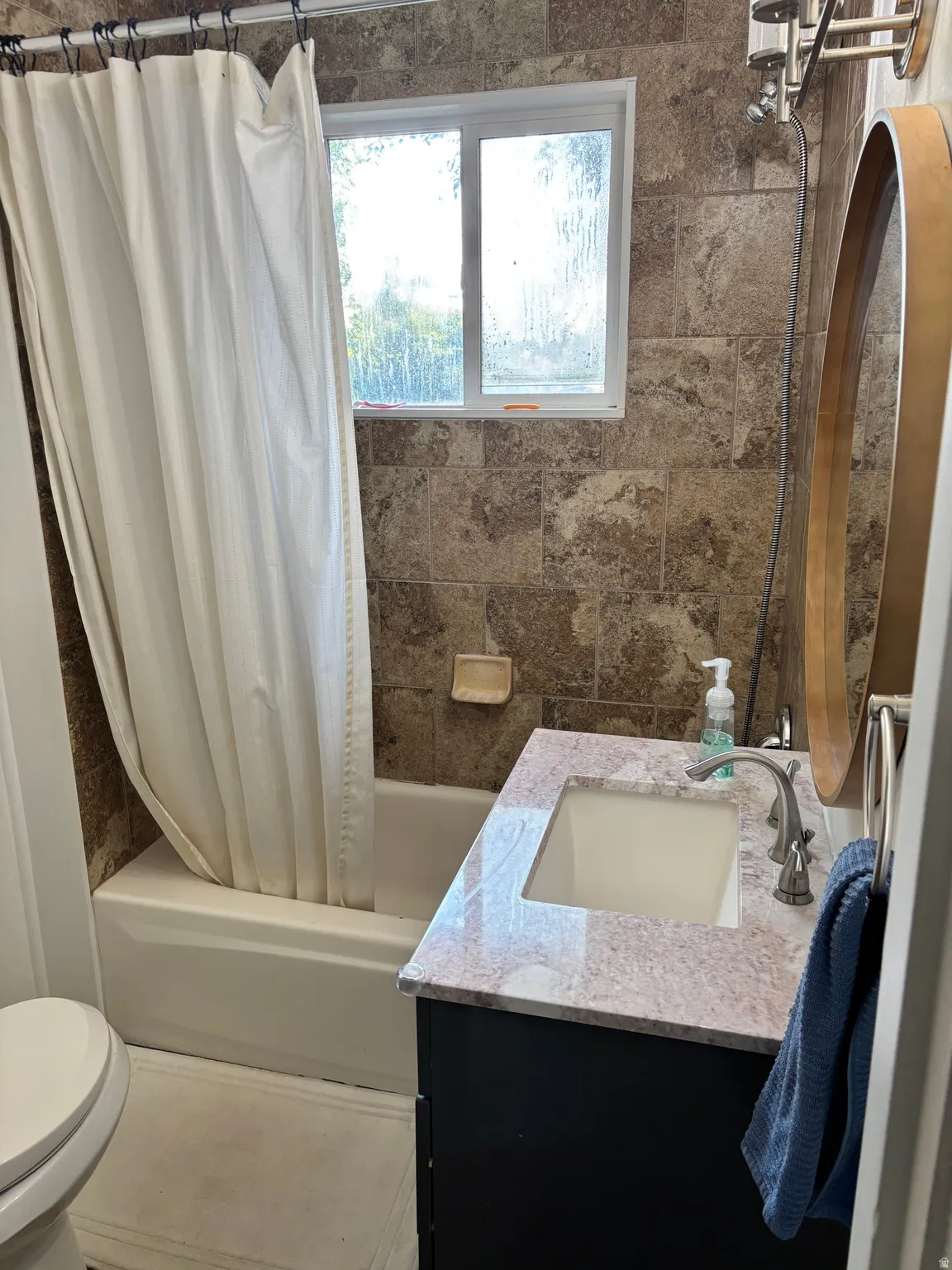 Tiled shower surround with an integrated bathtub, a single pane window, and a vanity featuring a granite countertop with an integrated sink