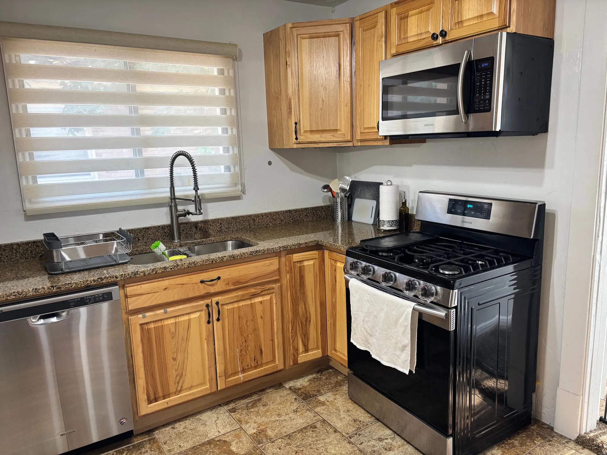 Kitchen featuring wood-finish cabinetry, stainless steel appliances, a double basin sink with a gooseneck faucet, and stone-finish countertops