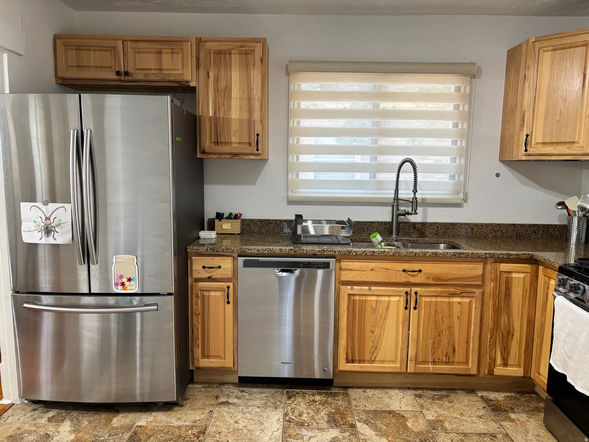 Stainless steel refrigerator, stainless steel dishwasher, wood-finish cabinetry, stone-finish countertops, and a gooseneck faucet