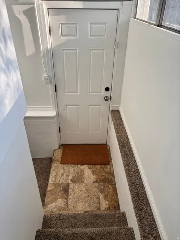 Six-panel entry door with polished hardware, textured tile flooring, and carpeted stairs