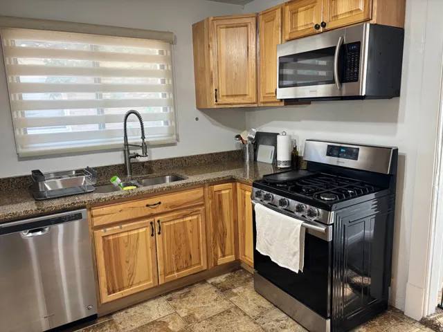 Kitchen featuring wood-finish cabinetry, stainless steel appliances, a double basin sink with a gooseneck faucet, and stone-finish countertops