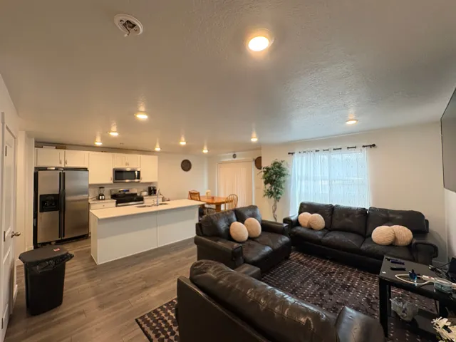 Open-concept living area featuring wood-finish flooring, recessed lighting, white cabinetry, stainless steel appliances, and a kitchen island with seating