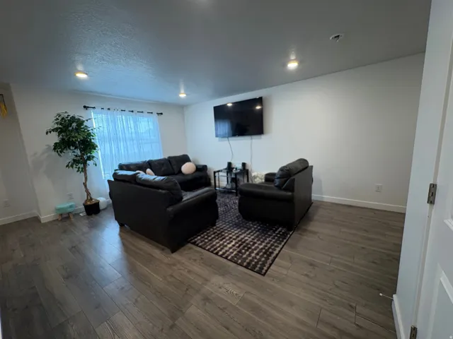 Recessed ceiling lighting, wood-finish flooring, white walls, and a window with curtain rod