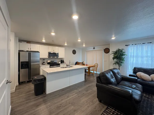 Open-concept kitchen with white cabinetry and stainless steel appliances, central island with seating, wood-finish flooring, and recessed lighting throughout