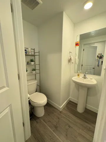 Pedestal sink, wall-mounted mirror, wood-finish flooring, recessed lighting, and a white toilet