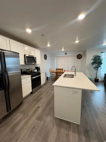 Kitchen featuring a large island with an undermount sink, stainless steel appliances, white cabinetry, and wood-finish flooring