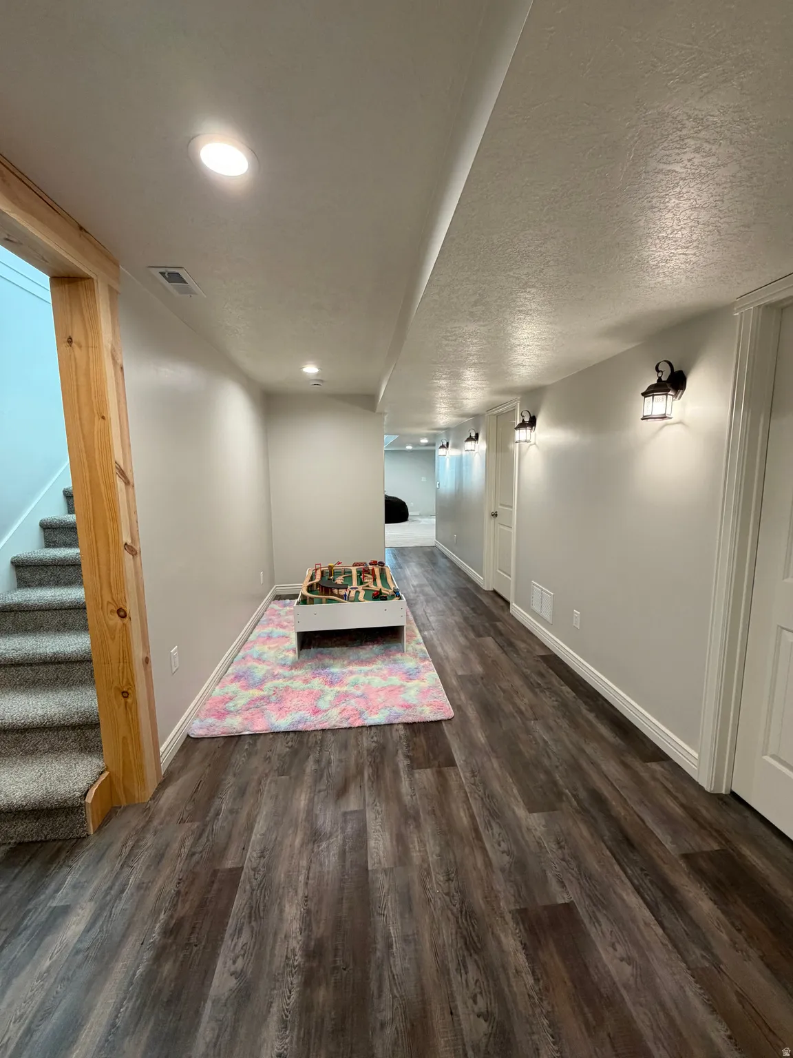 Large open basement hallway with LVP flooring,  recessed ceiling lights, and multiple wall sconces provide ample illumination