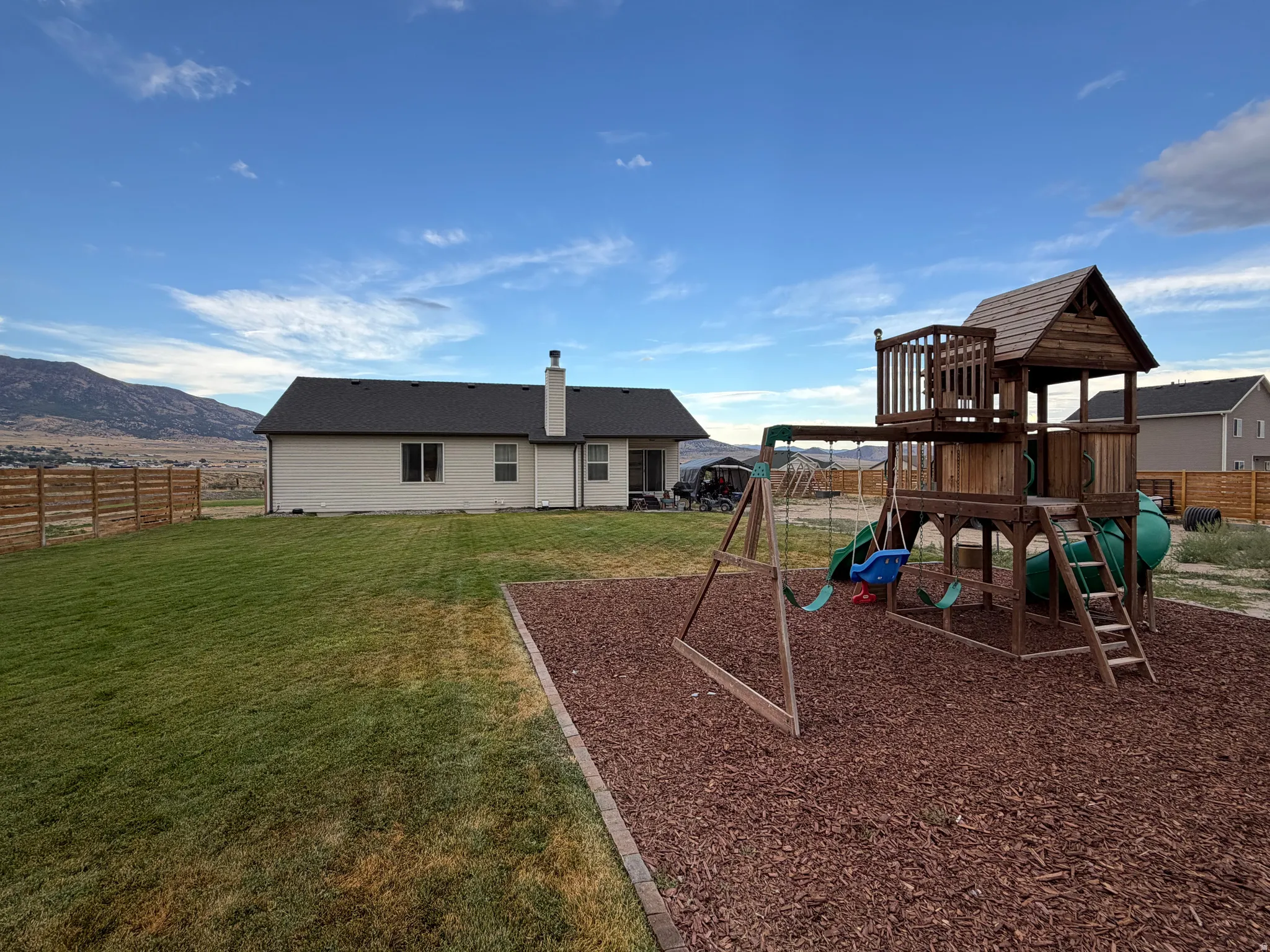 Expansive backyard featuring a manicured lawn, a wooden playset on a bark-mulch surface.