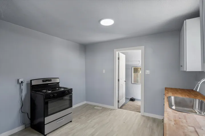 Stainless steel gas range, wood-finish flooring, white cabinetry, circular ceiling light, and a stainless steel sink