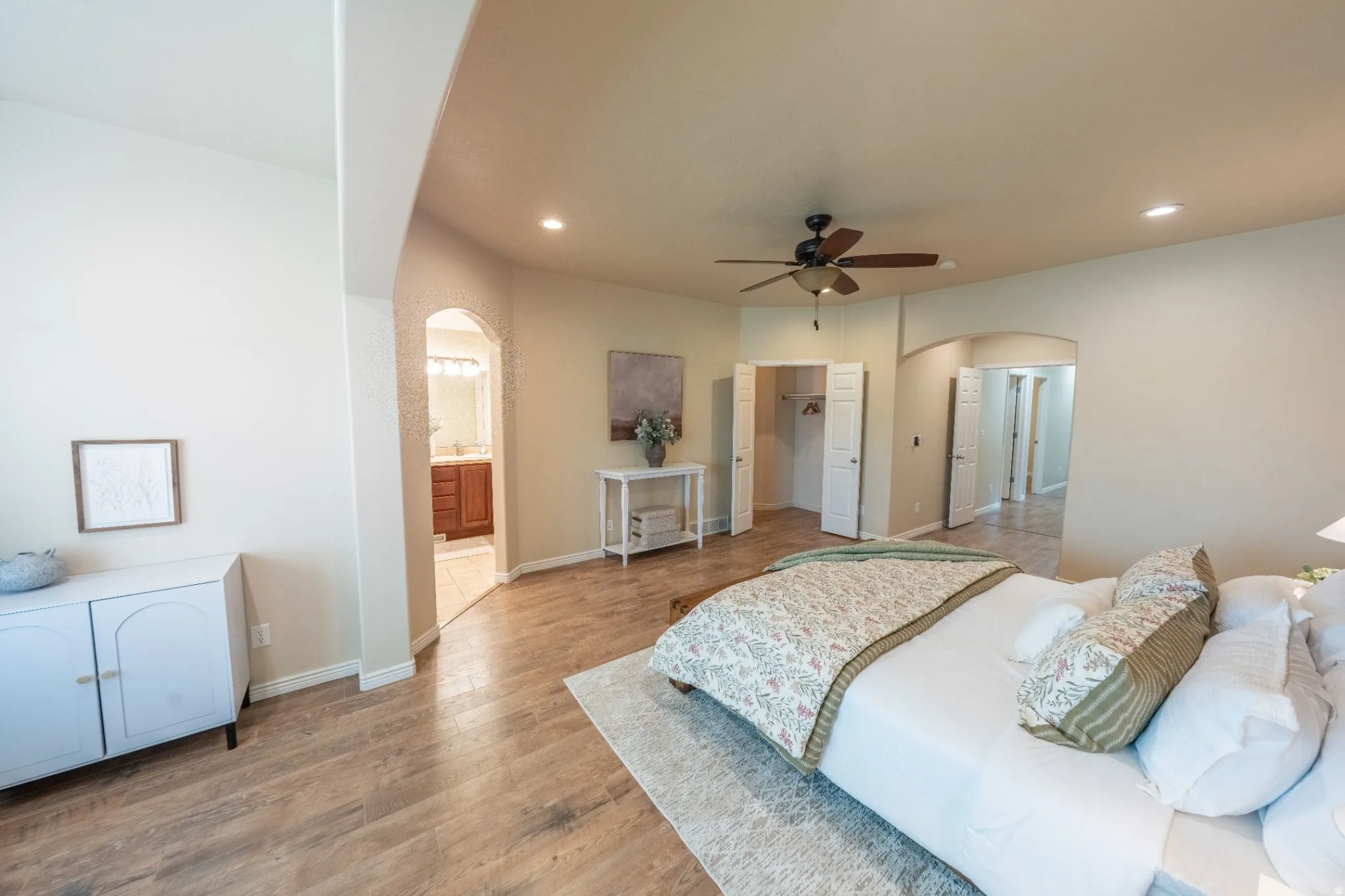 Wood-finish flooring throughout, recessed lighting, and an arched doorway leading to a built-in vanity with wood cabinetry