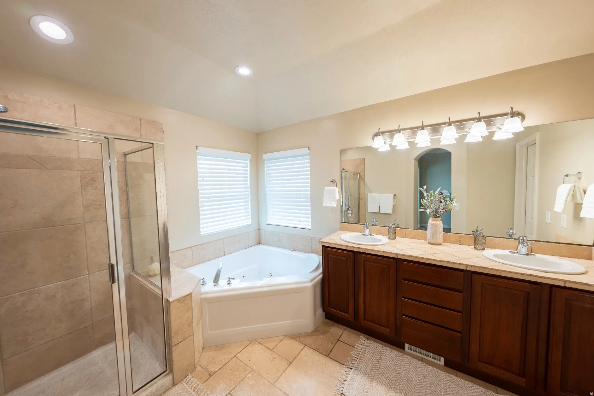 Dual vanity with undermount sinks, corner jetted tub, tiled walk-in shower with glass enclosure, and recessed lighting