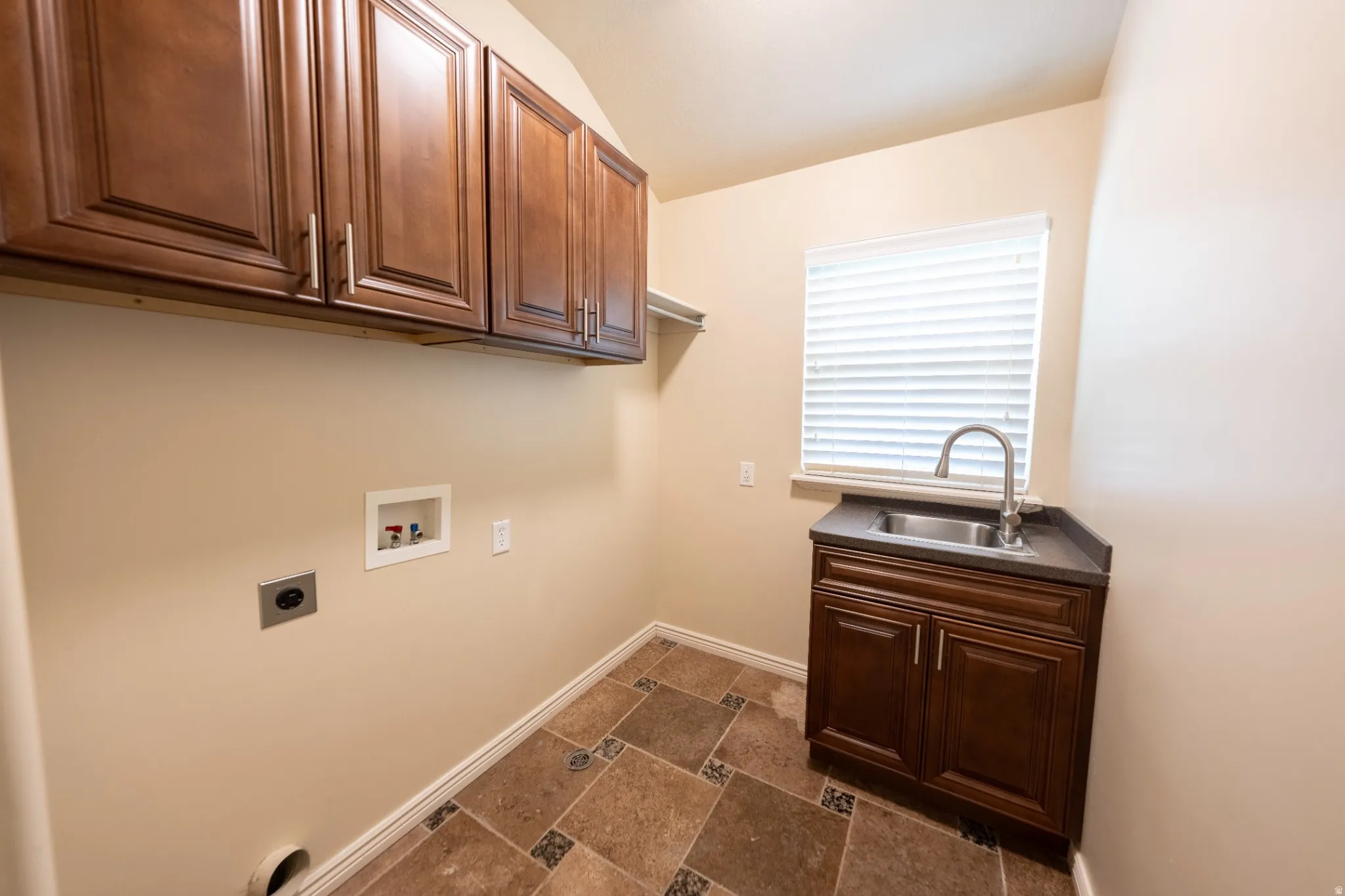 Laundry room featuring multi-toned tile flooring, dark wood cabinetry, a stainless steel sink with a gooseneck faucet, and a window with blinds
