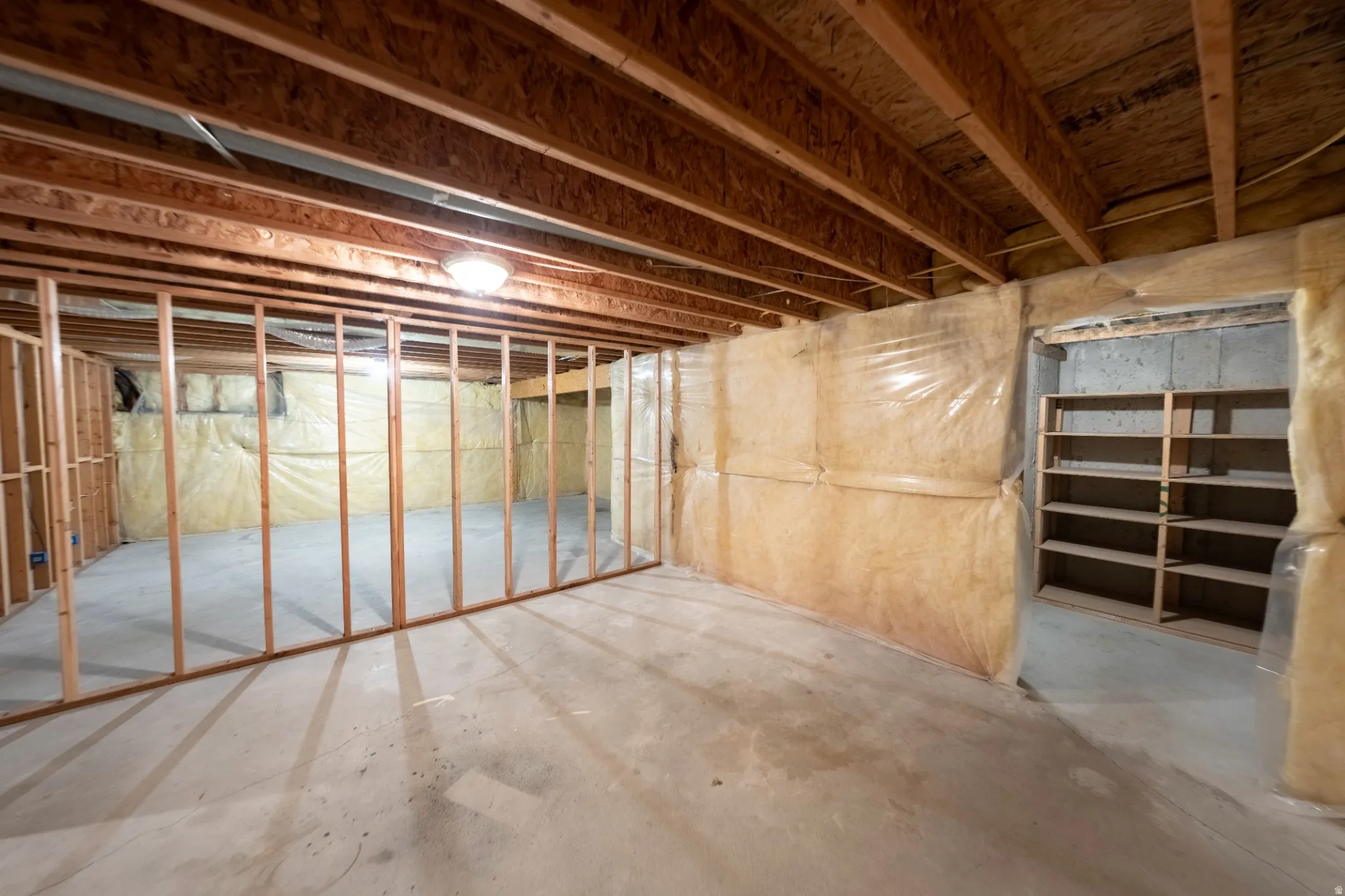 Unfinished basement with exposed wood framing, concrete flooring, insulated walls, built-in shelving, and exposed ceiling joists