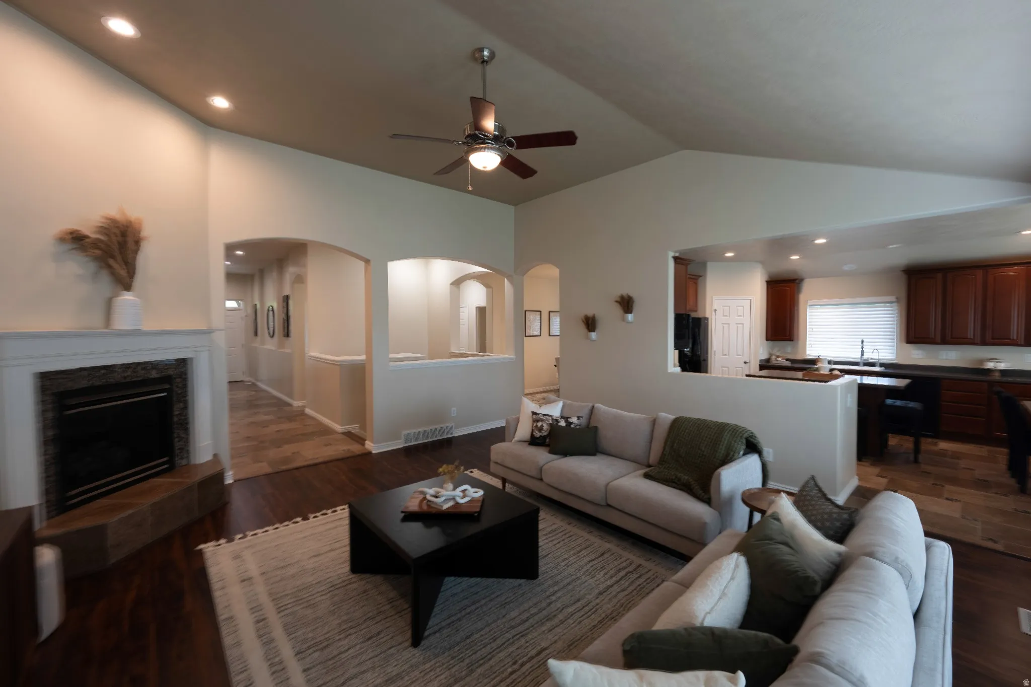 Vaulted ceilings, recessed lighting, wood-finish flooring, a built-in fireplace with a tiled surround, and arched doorways