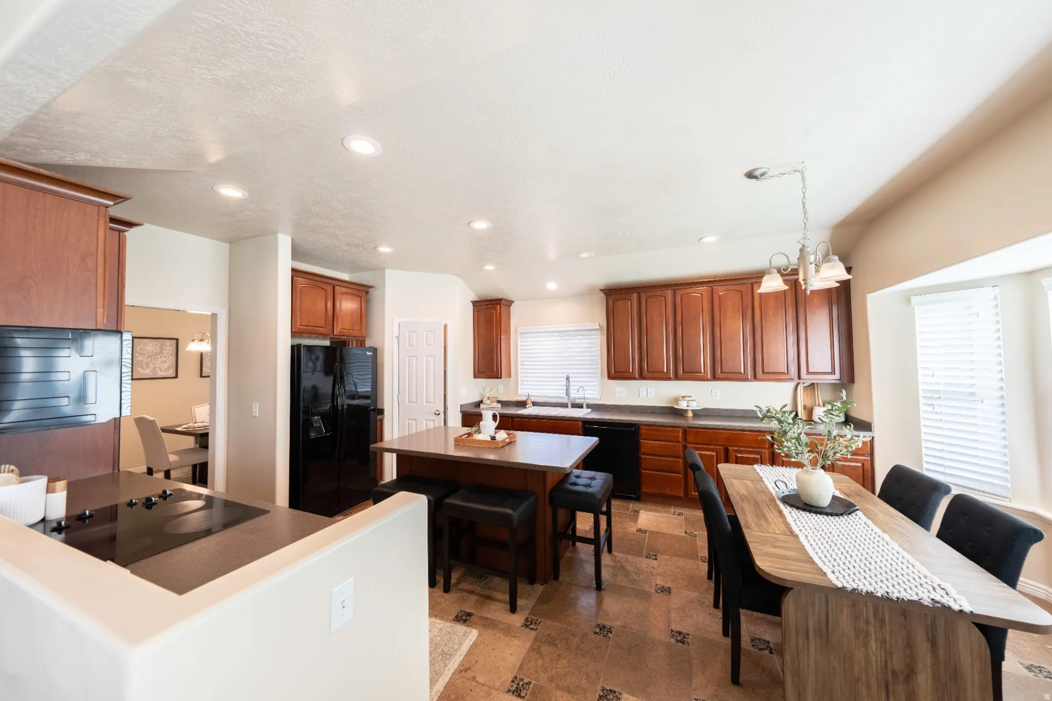 Kitchen featuring wood-finish cabinetry, black appliances, recessed lighting, a center island, and tiled flooring