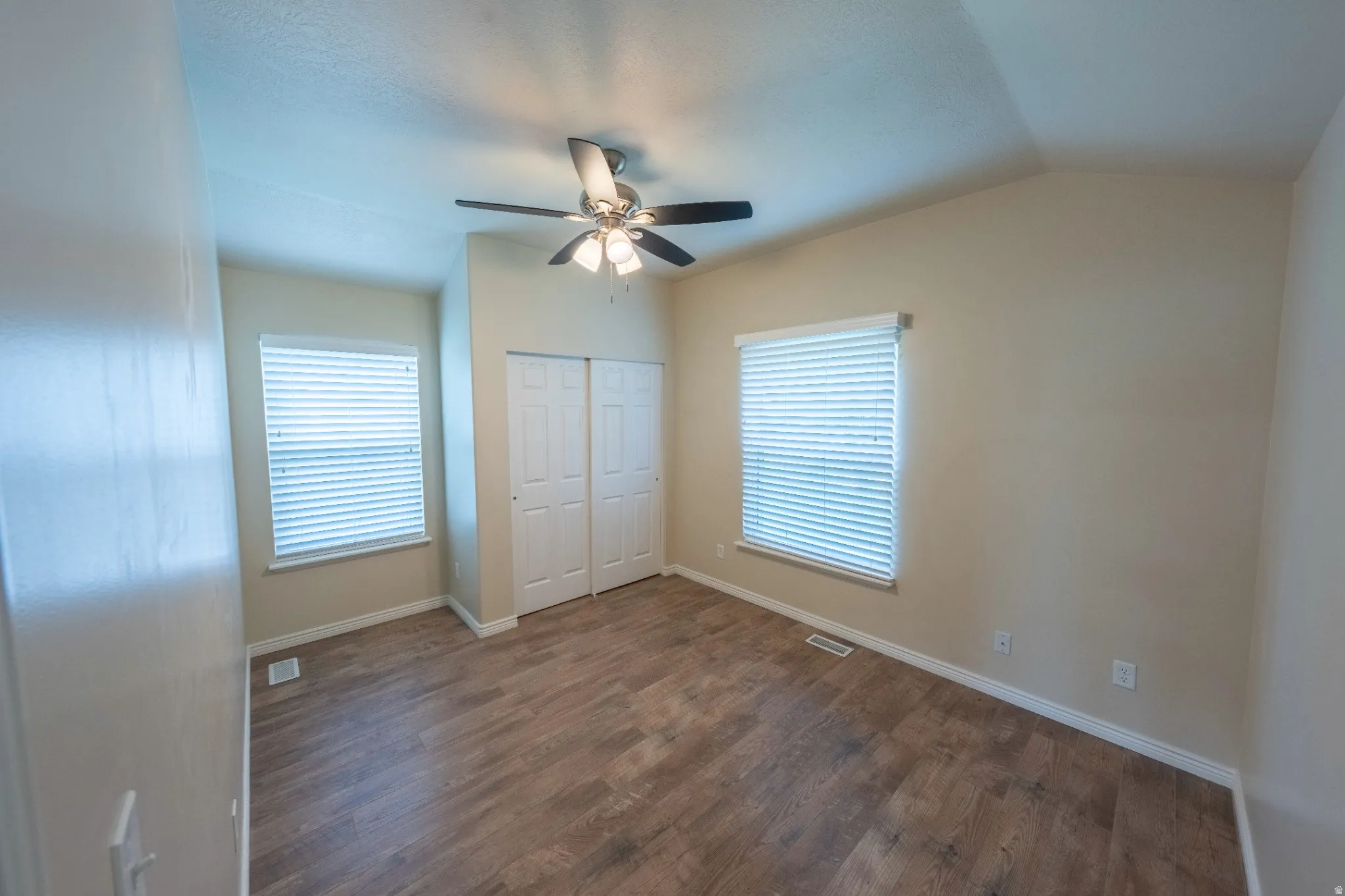Wood-finish flooring, vaulted ceiling, dual windows with blinds, and a ceiling fan with integrated lighting