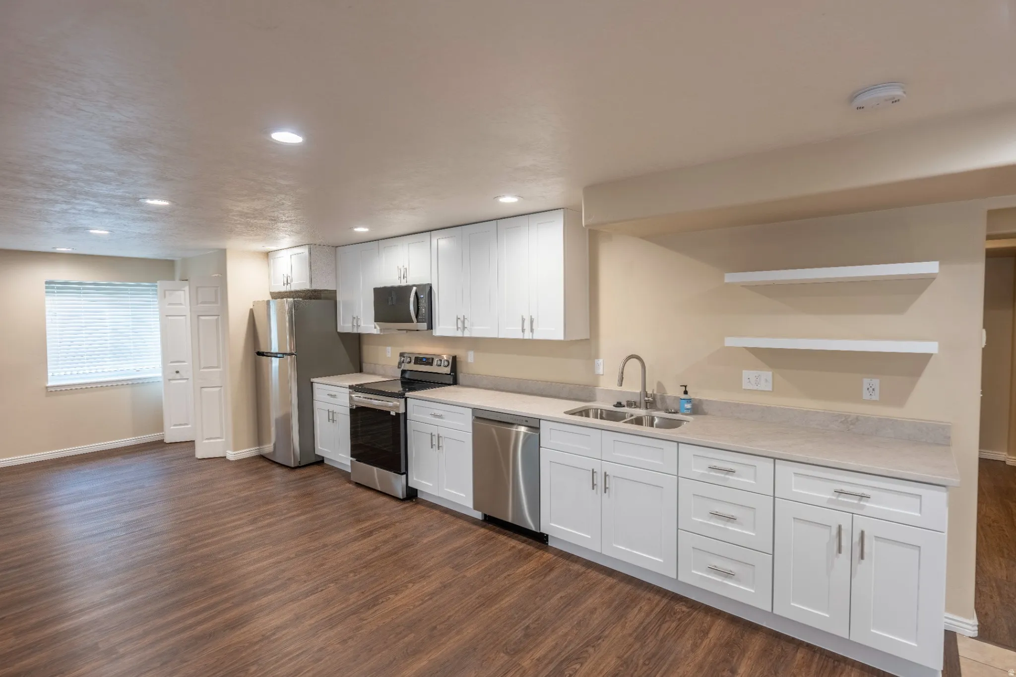 Kitchen featuring white cabinetry with silver hardware, stainless steel appliances, wood-finish flooring, and recessed lighting