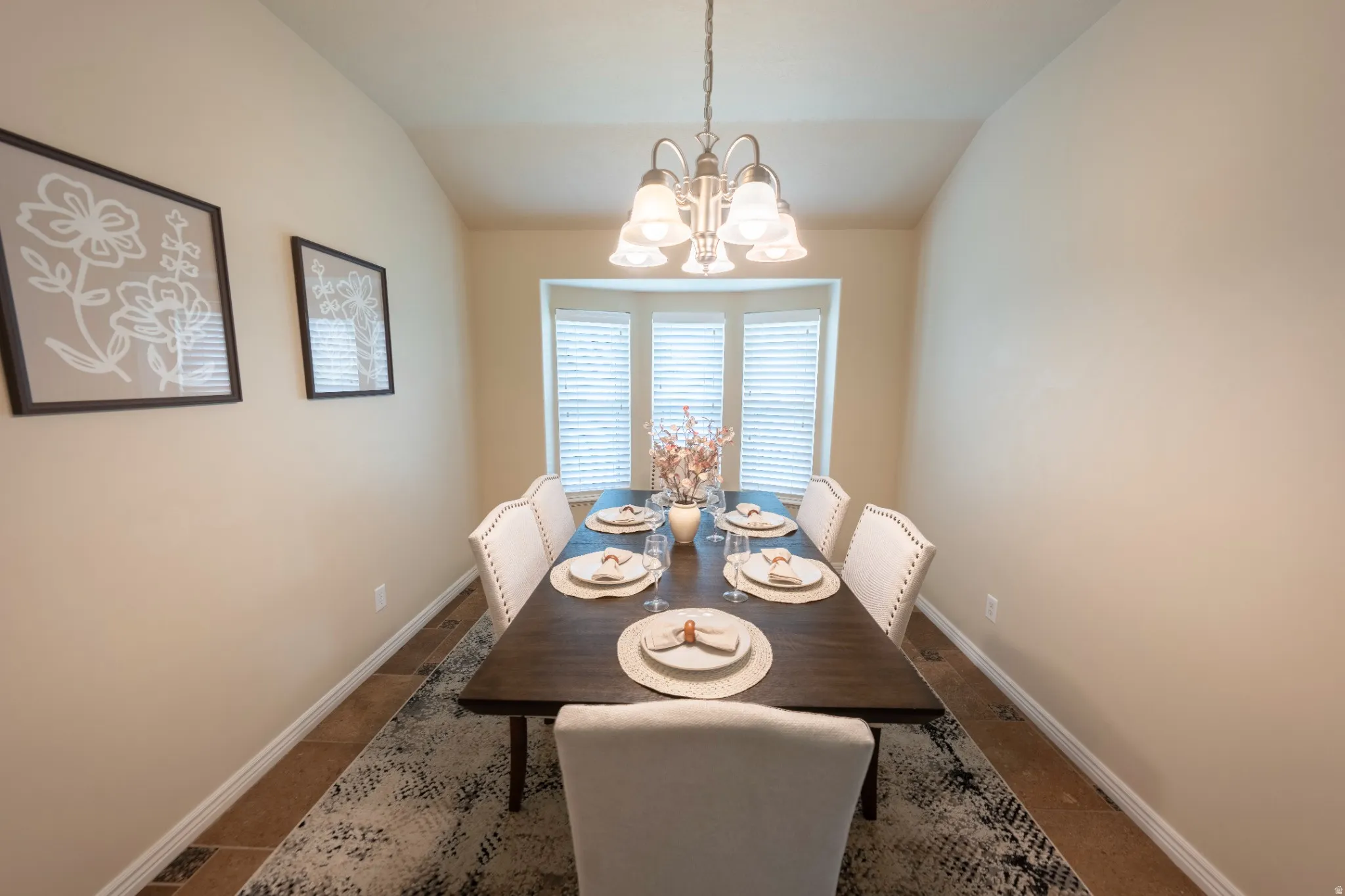 Vaulted ceiling with a pendant light fixture, bay window with blinds, wood-finish flooring, and neutral wall tones