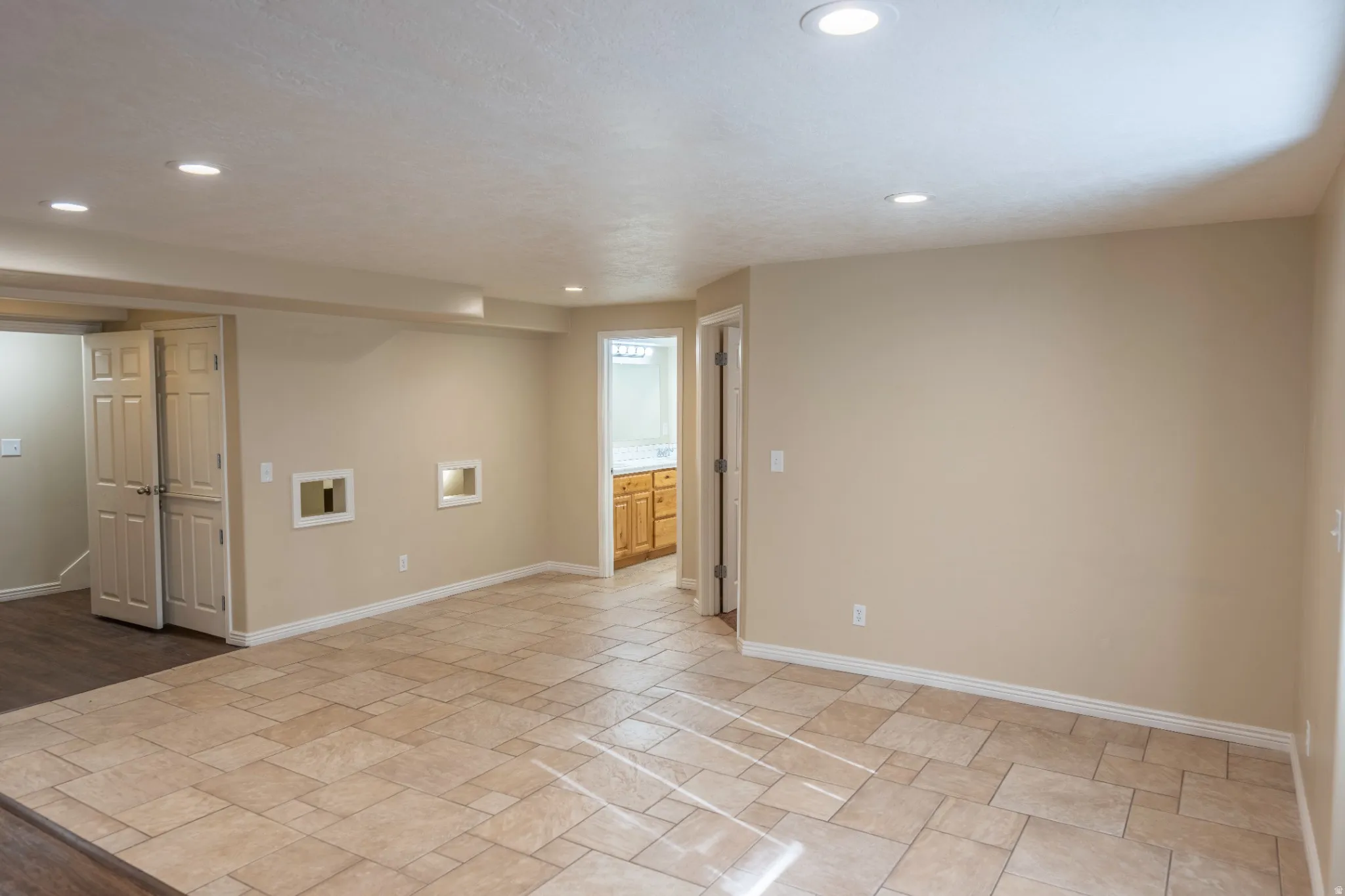 Recessed lighting, tile flooring, wood-finish flooring, paneled bifold doors, and a partial view of a room with wood cabinetry