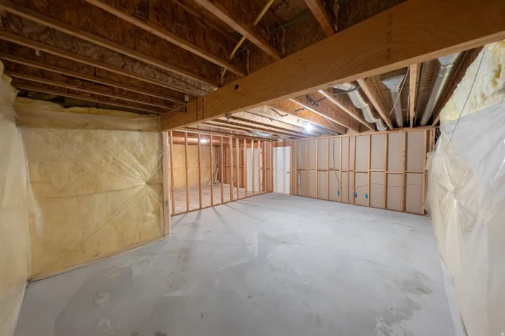 Unfinished basement featuring exposed wood framing, concrete flooring, and partial wall insulation