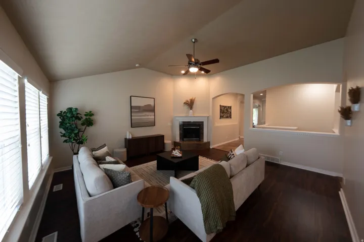 Vaulted ceiling, dark wood-finish flooring, fireplace, ceiling fan, and architectural arched openings