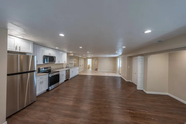 Spacious open-concept area featuring wood-finish flooring, recessed lighting, and a kitchen with white cabinetry and stainless steel appliances