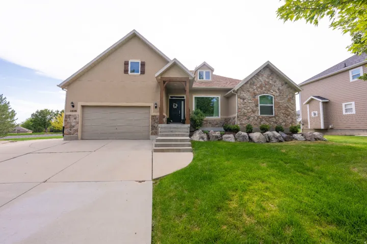 Stucco and stone exterior featuring multiple gables, an attached garage, and a concrete driveway