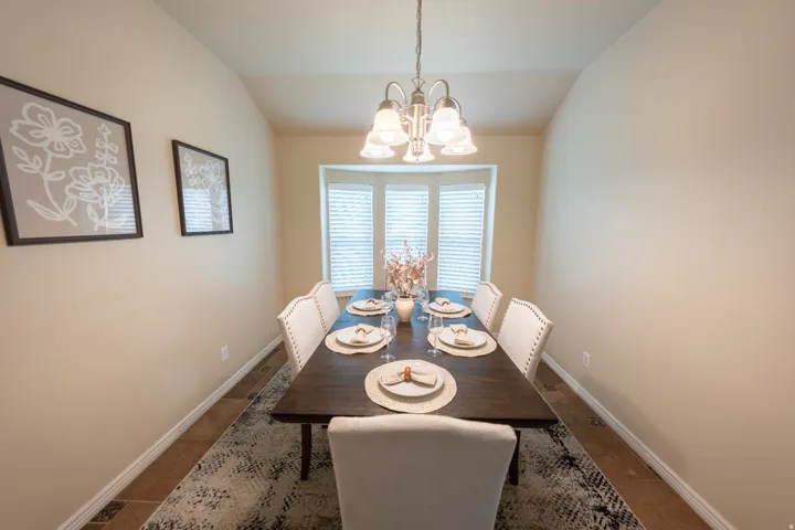 Vaulted ceiling with a pendant light fixture, bay window with blinds, wood-finish flooring, and neutral wall tones
