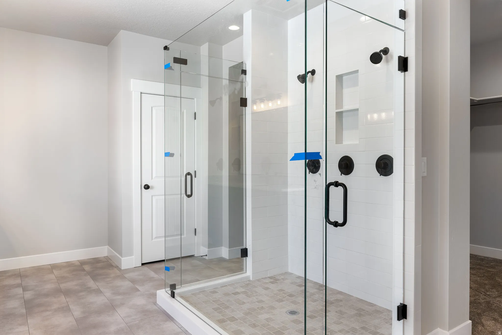 Walk-in shower with clear glass enclosure and matte black fixtures, integrated shelving, and tiled flooring