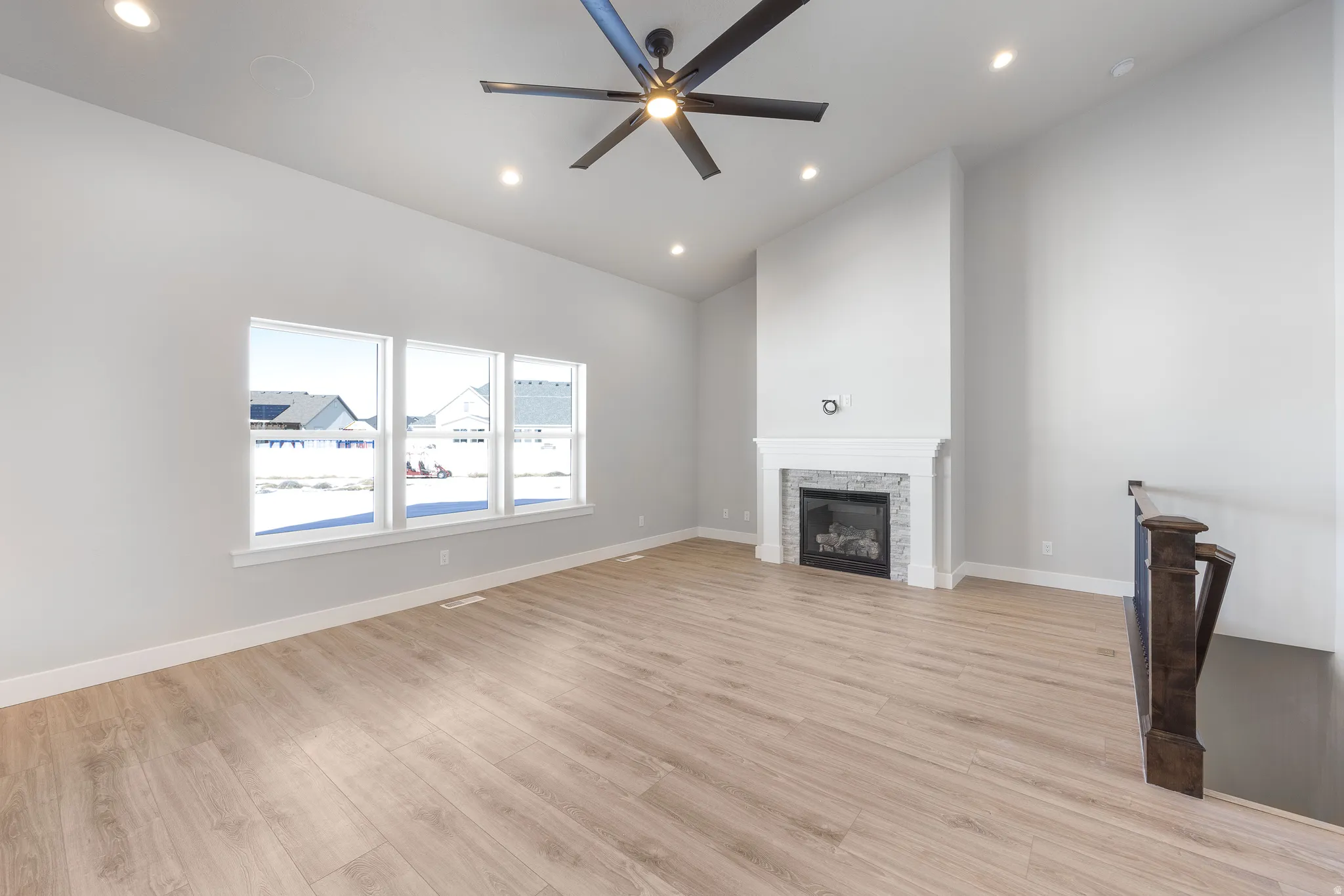 Vaulted ceilings, wood-finish flooring, recessed lighting, and a fireplace with a decorative mantel and stone surround