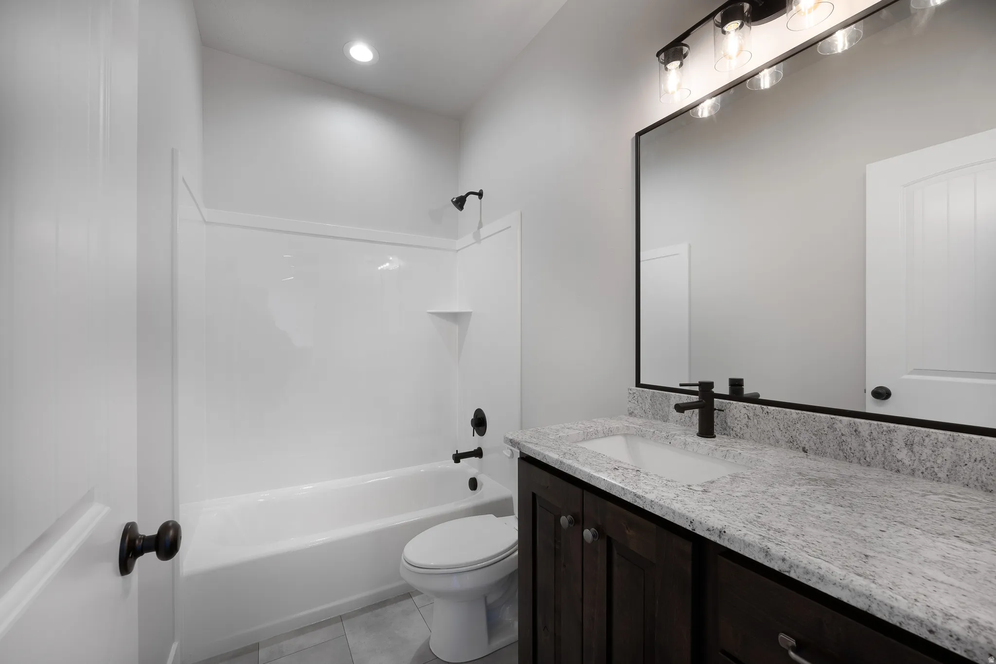 Granite-finish countertop, dark wood-finish vanity, large framed mirror, and a full bathtub with shower