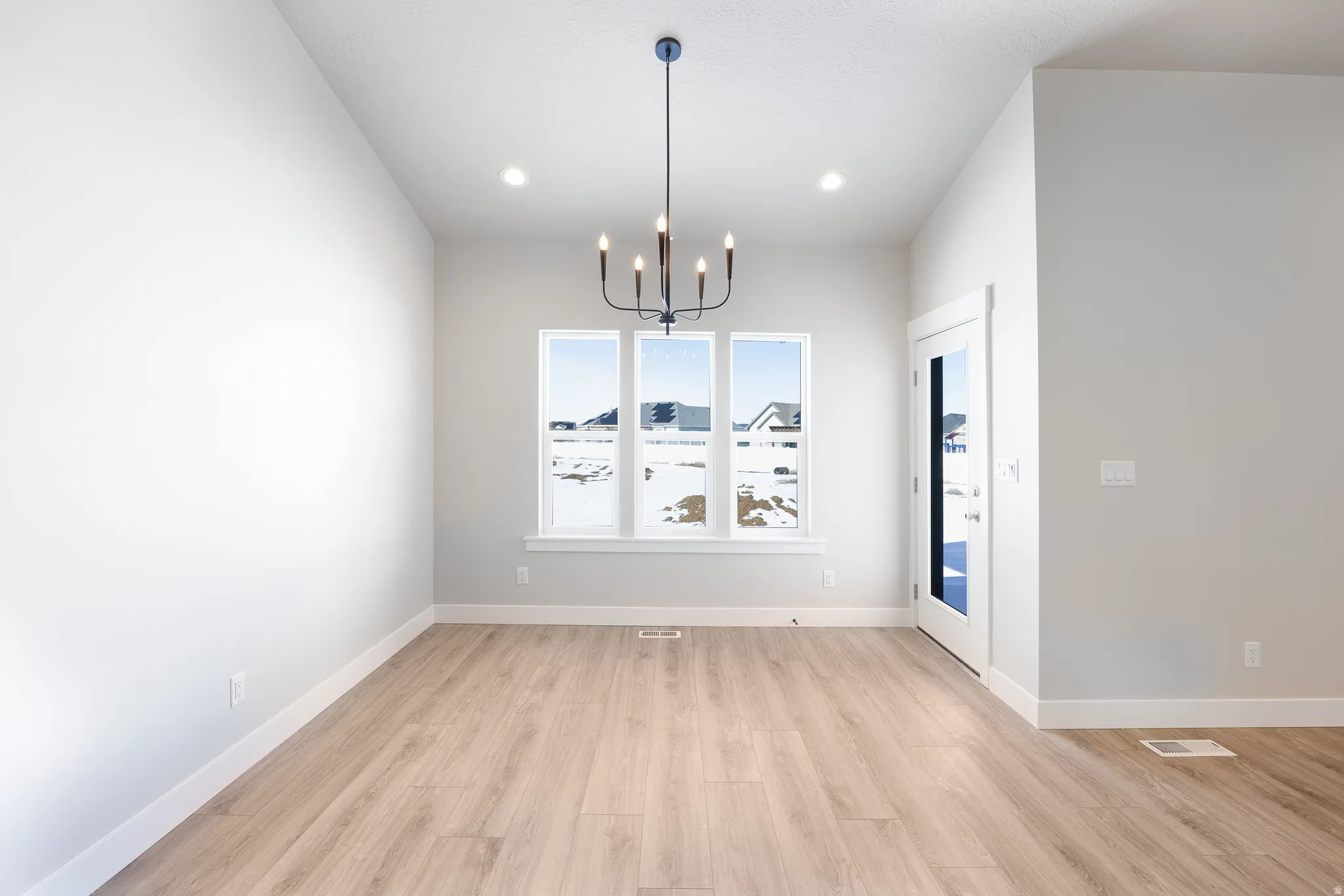 Vaulted ceiling with recessed lighting, black finish chandelier, wood-finish flooring, and multiple pane windows