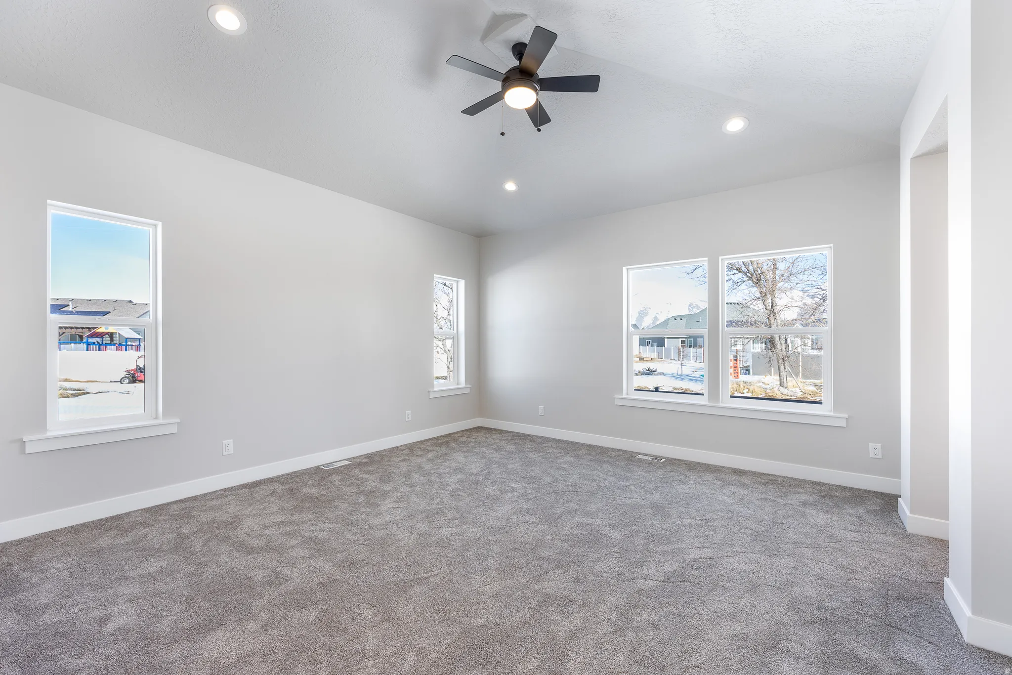 Vaulted ceiling, recessed lighting, ceiling fan, multiple windows, and gray carpet flooring