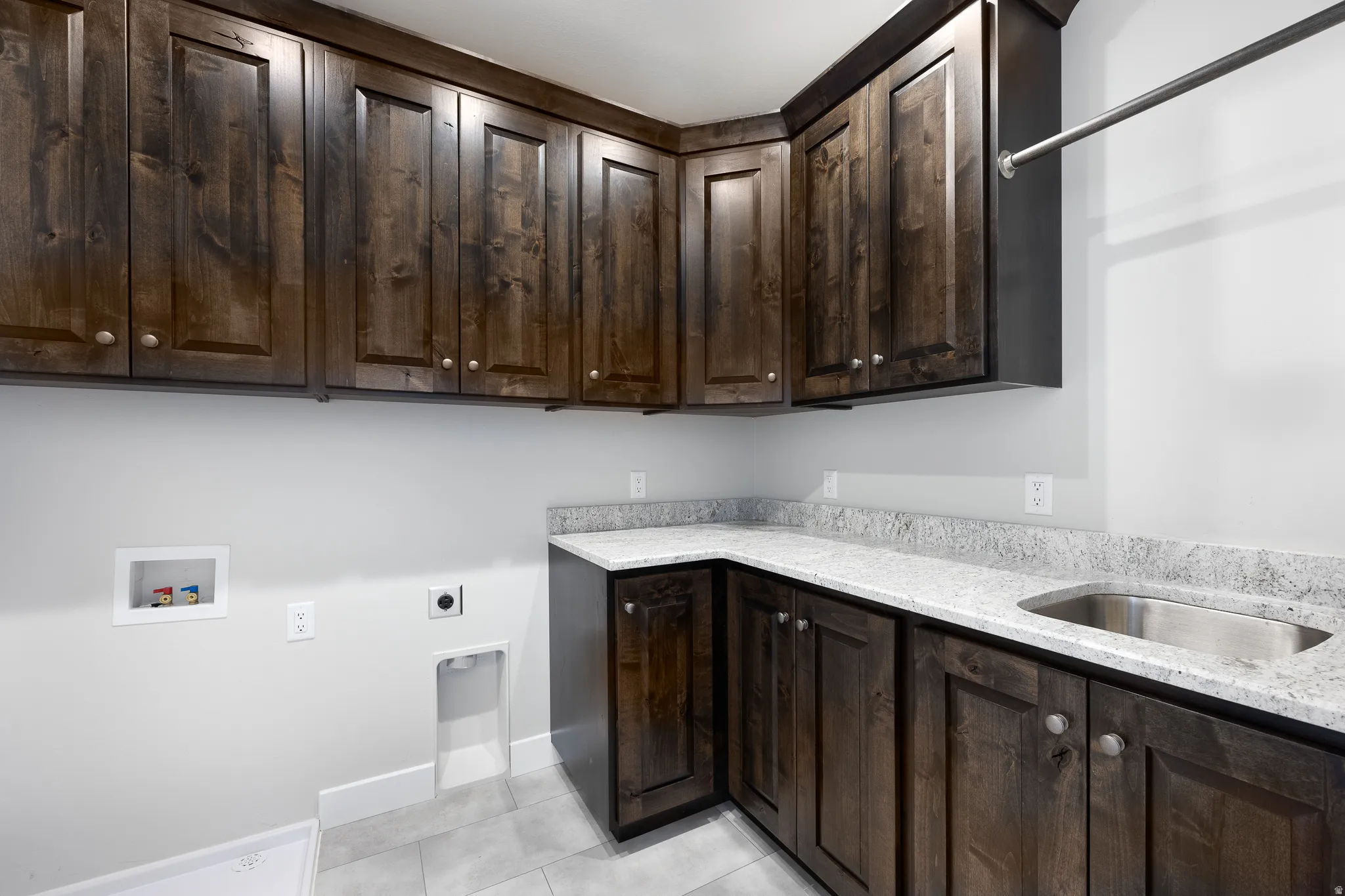 Extensive dark wood cabinetry with brushed nickel hardware, light-toned stone-finish countertops, stainless steel undermount sink, and a built-in hanging rod