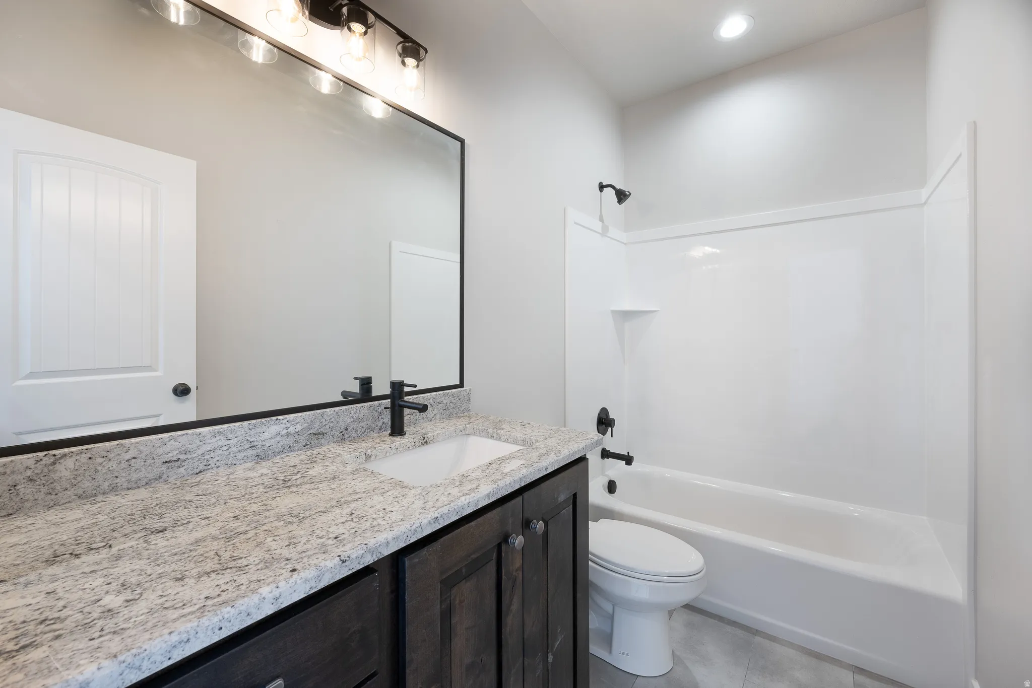 White tub and shower combination with dark bronze fixtures, a vanity with a white countertop and integrated sink, dark wood-finish cabinetry, and a large wall-mounted mirror