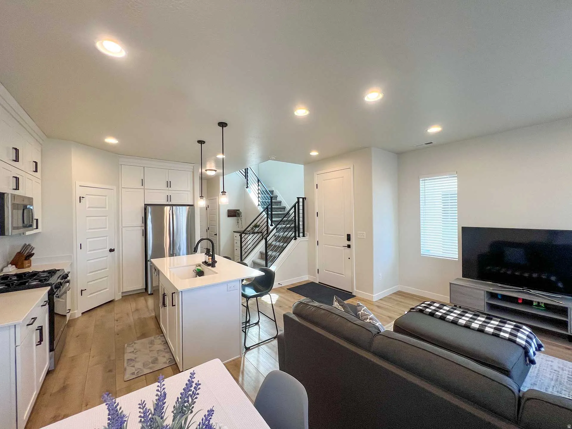 Open-concept living space featuring a kitchen island with seating, stainless steel appliances, wood-finish flooring, a contemporary staircase with iron railings, and recessed lighting throughout