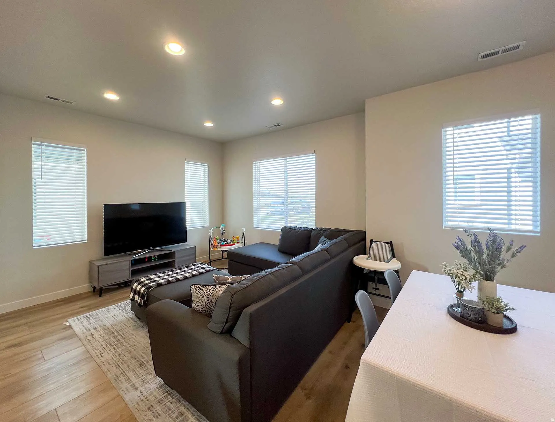 Recessed lighting throughout, multiple windows with blinds, light neutral wall paint, and wood-finish flooring