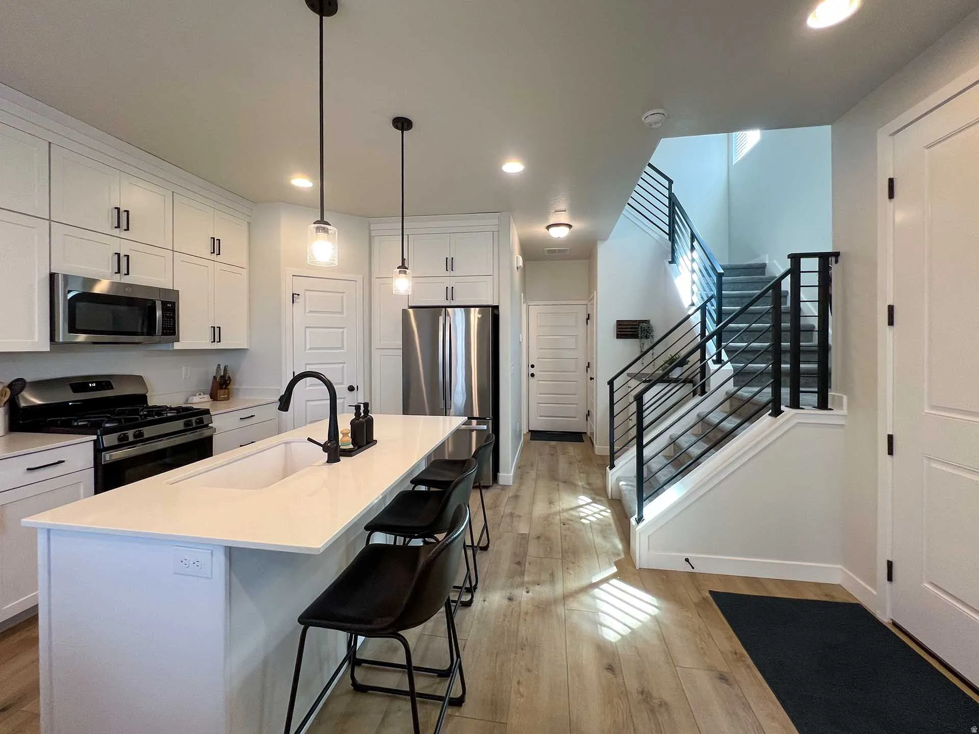 Kitchen featuring white cabinetry, stainless steel appliances, a center island with sink, and pendant lighting
