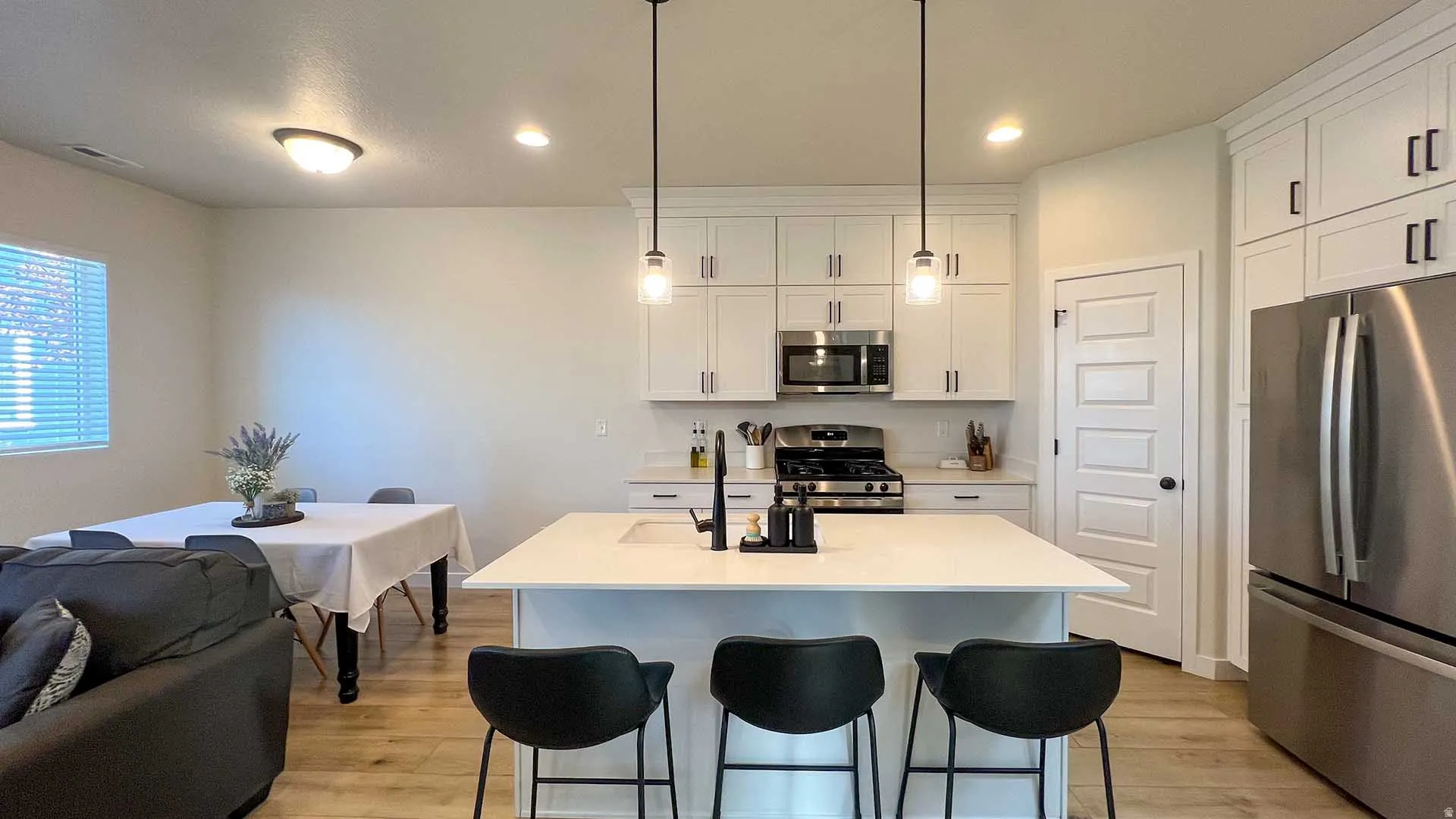 Kitchen featuring white cabinetry, stainless steel appliances, a center island with sink, and wood-finish flooring
