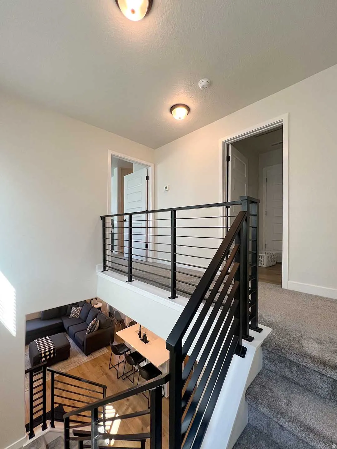 Open-concept living space with wood-finish flooring, black metal railing, and carpeted stairs