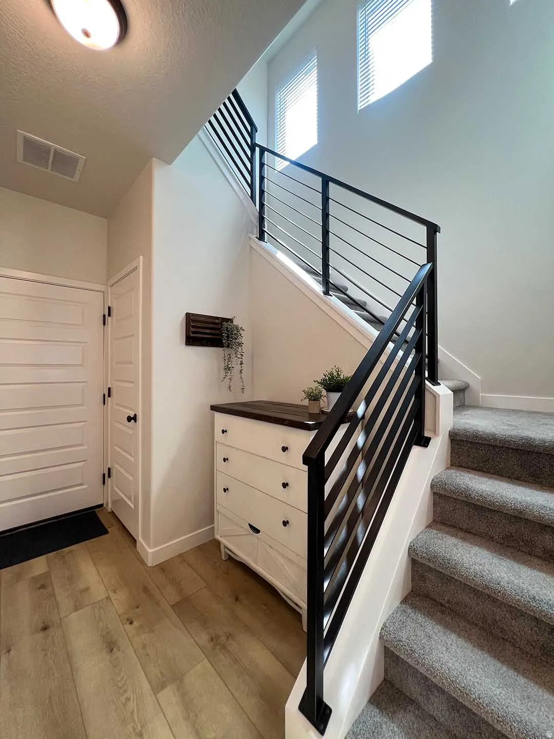 Two-story entry featuring light wood-finish flooring, a contemporary staircase with black horizontal balusters, and a solid white door