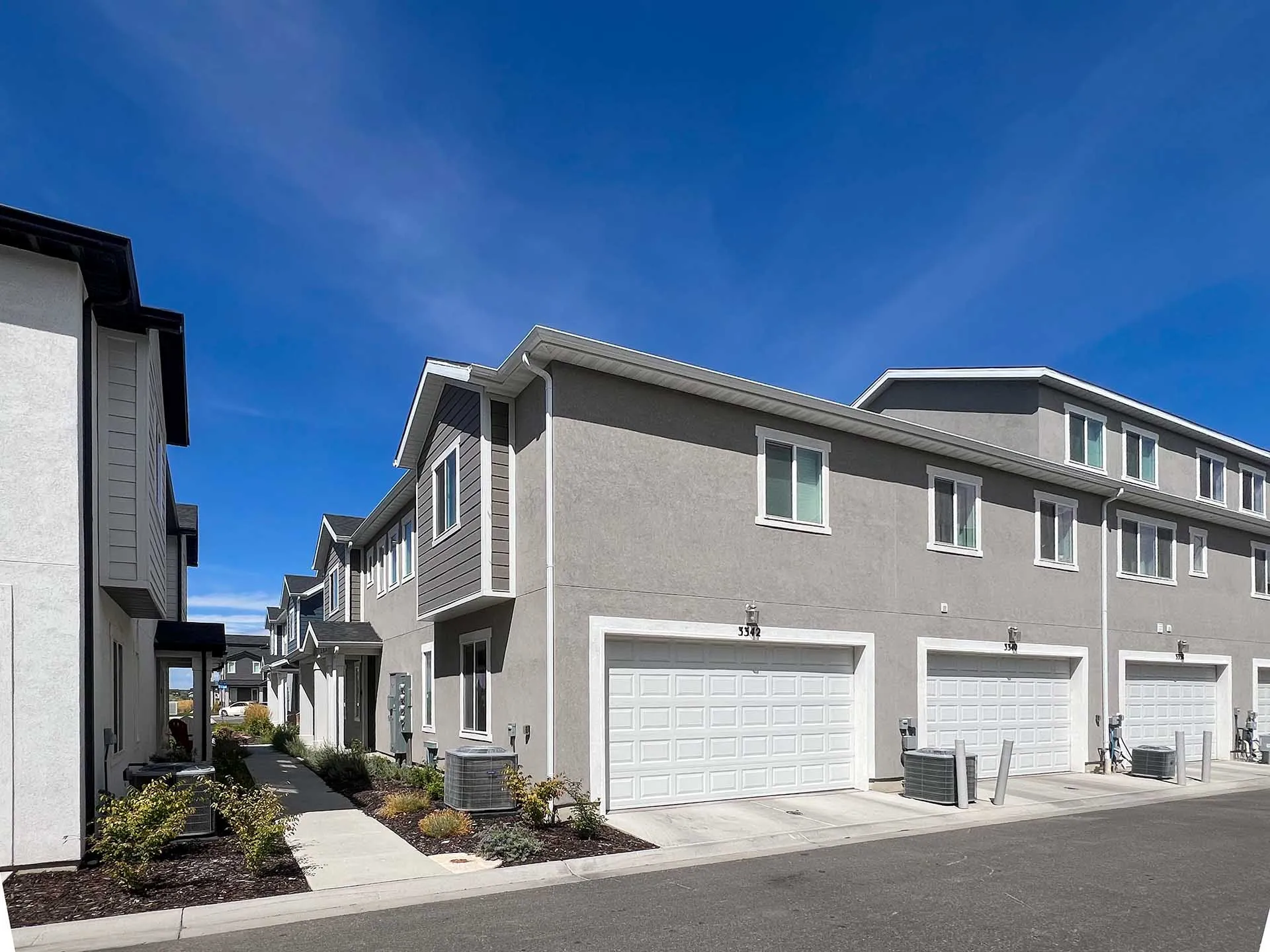 Contemporary multi-story exterior with stucco and horizontal siding, individual garage doors, and landscaped walkways
