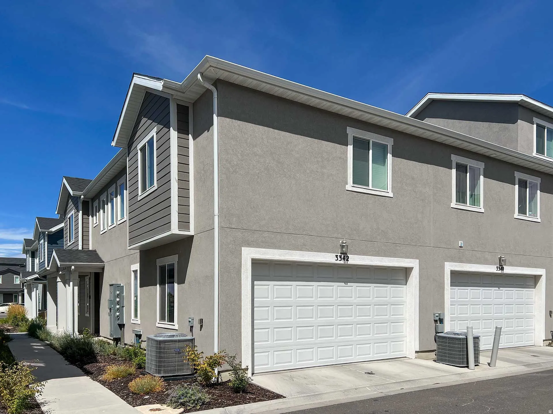 Stucco exterior with contrasting horizontal siding accents, white framed windows, and attached garage