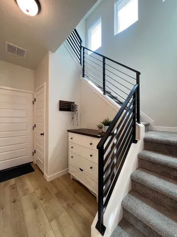 Two-story entry featuring light wood-finish flooring, a contemporary staircase with black horizontal balusters, and a solid white door