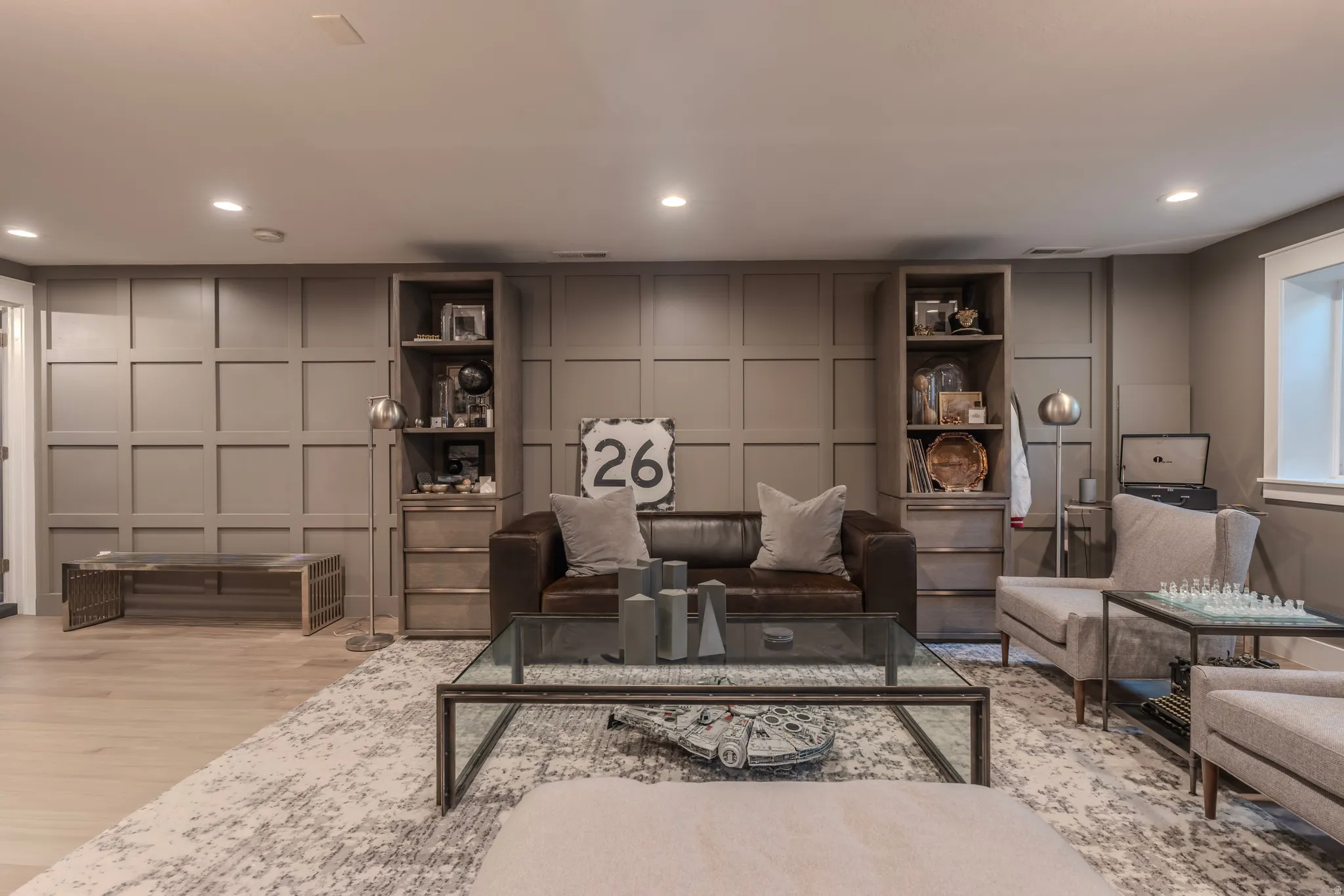 Recessed lighting, wood-finish flooring, accent wall with paneling, built-in shelving, and a glass-top coffee table