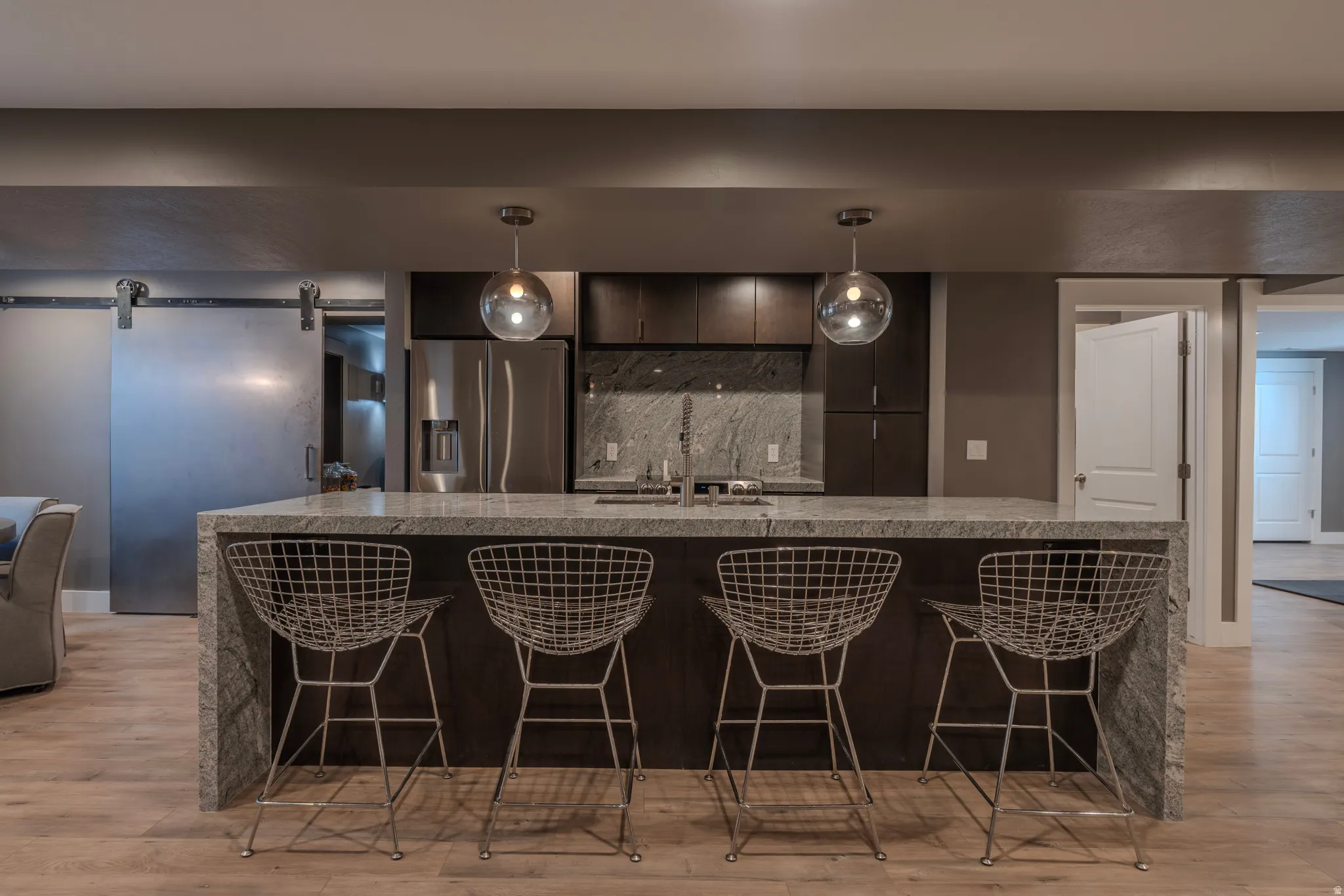 Kitchenette featuring a waterfall island, built-in sink, stainless steel refrigerator, and dark wood-finish cabinetry