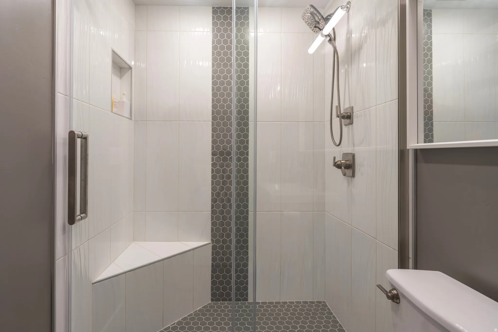 Glass-enclosed shower with a built-in bench, hexagon tile flooring, a recessed niche, and a brushed nickel shower head
