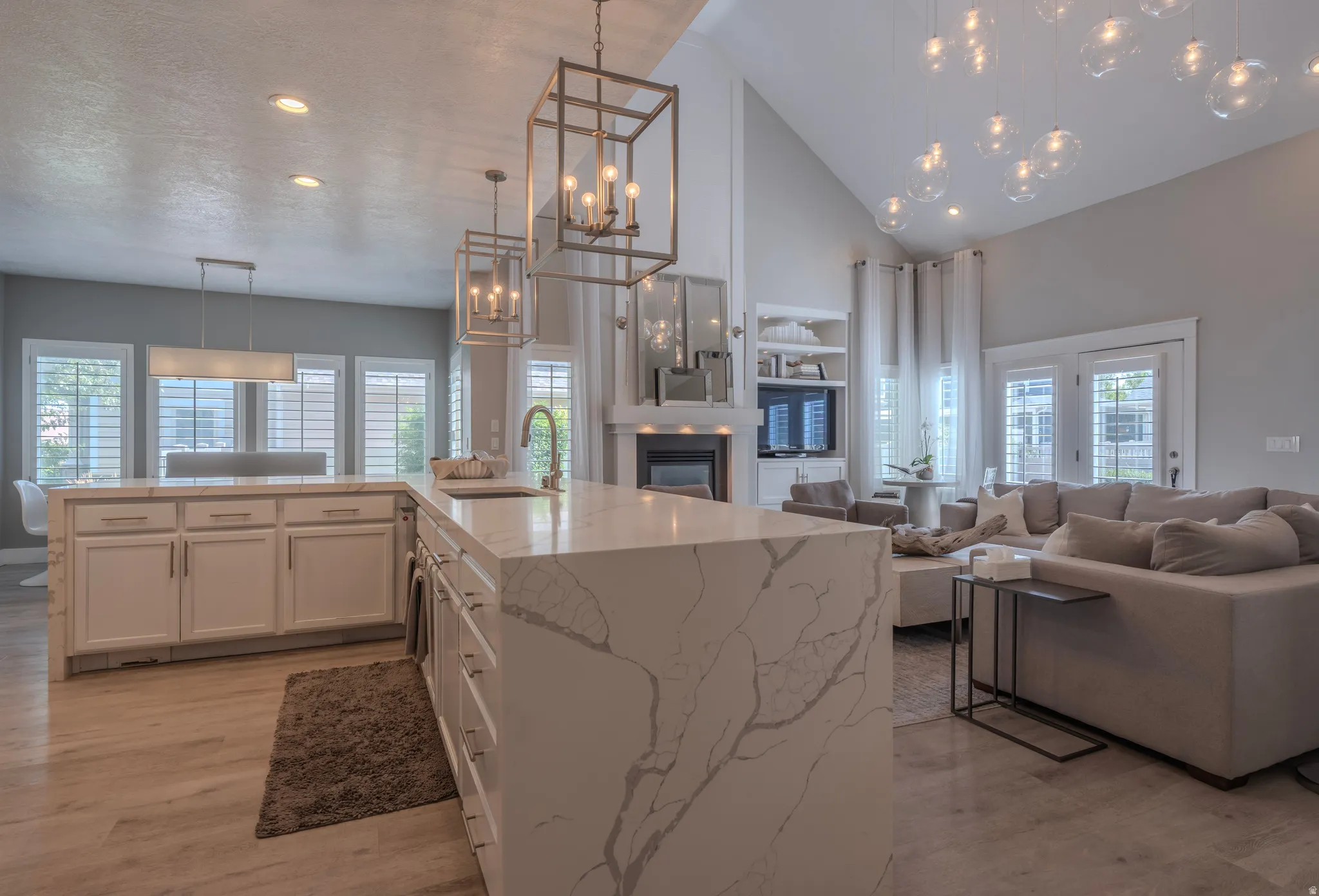 Kitchen island with waterfall countertop, wood-finish flooring, vaulted ceiling, built-in shelving, and French doors